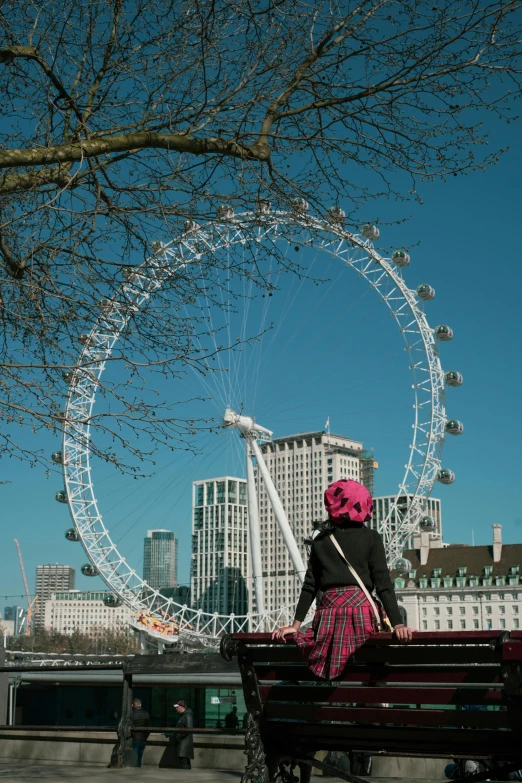 a woman is sitting on a bench and looking at a ferris wheel