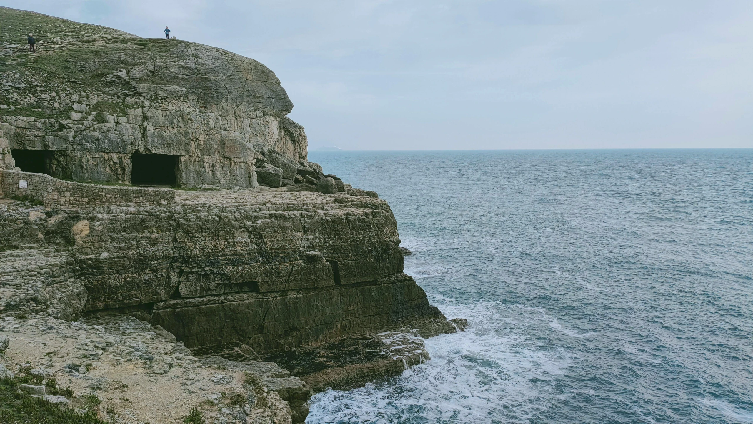 a cliff sitting next to the ocean with some small rocks in front