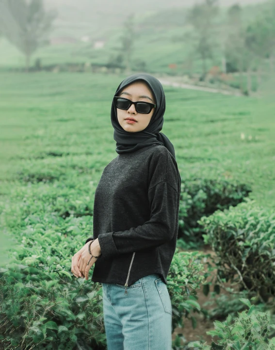 a woman stands in a field with sunglasses on