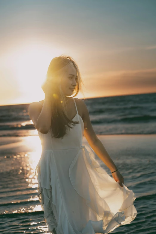 a young woman in white walking on the beach at sunset