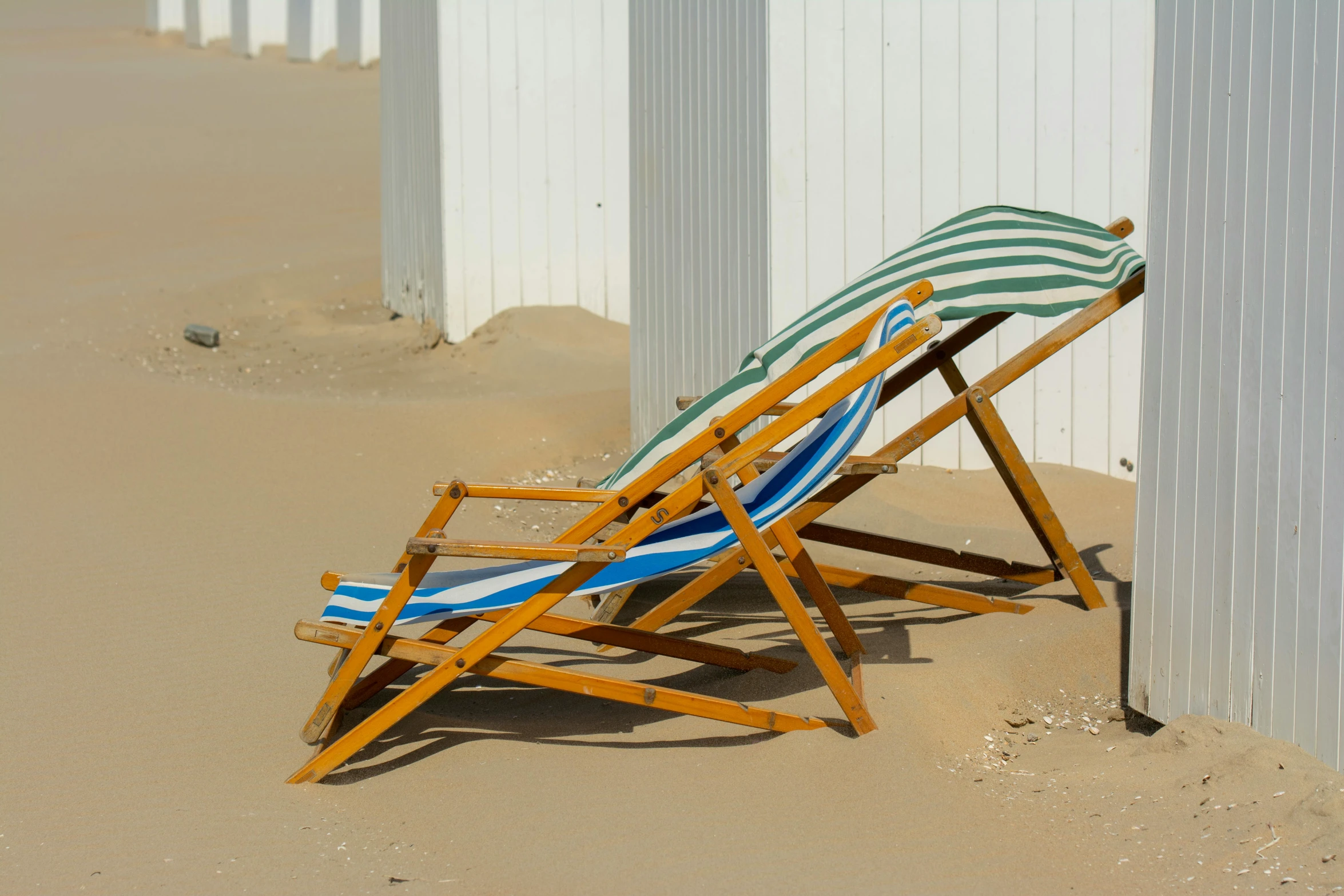 a wooden beach chair with striped seat beside wall