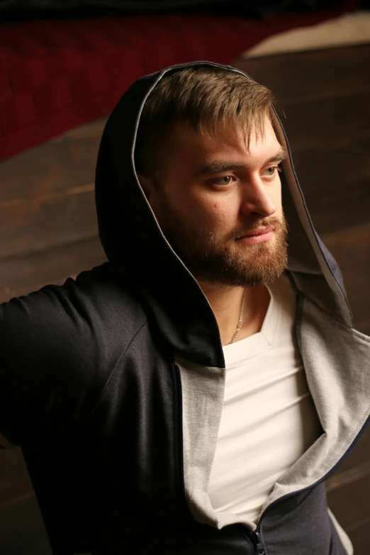 a man with a hood up sitting on a wooden floor