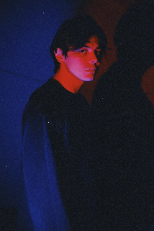 a boy standing up against a wall in the dark