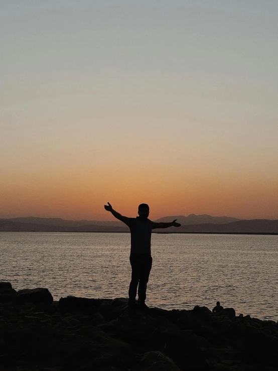 a person is standing near the water at sunset