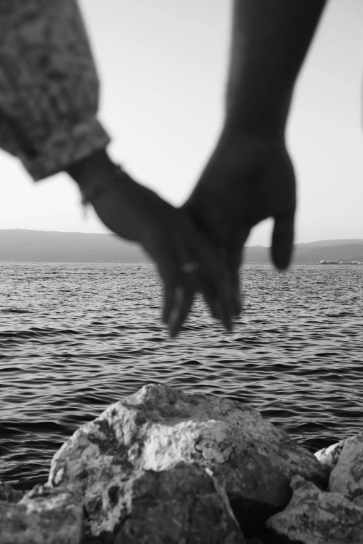 a couple holds hands above some rocks by the water