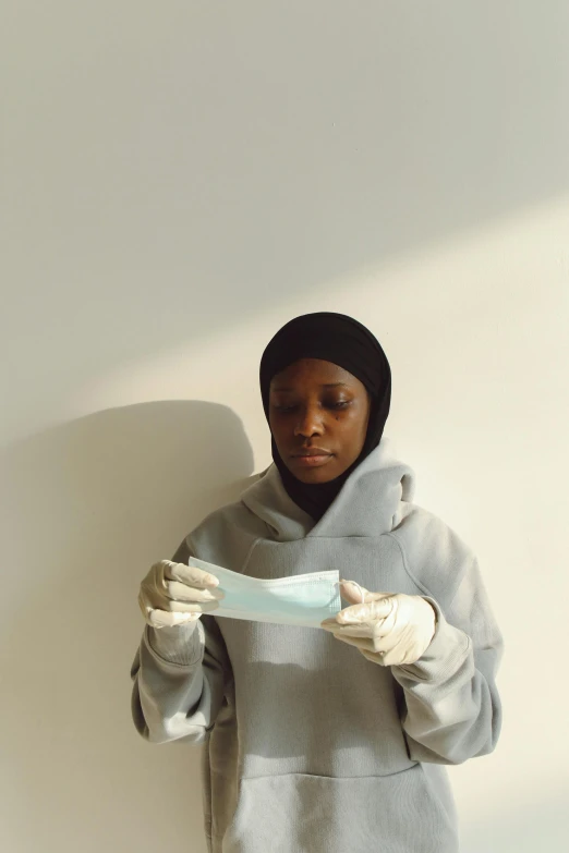 a young woman wearing a hoodie and gloves holds a piece of white paper