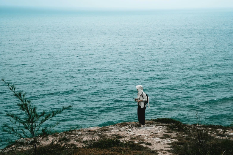 a woman standing on top of a cliff overlooking a body of water