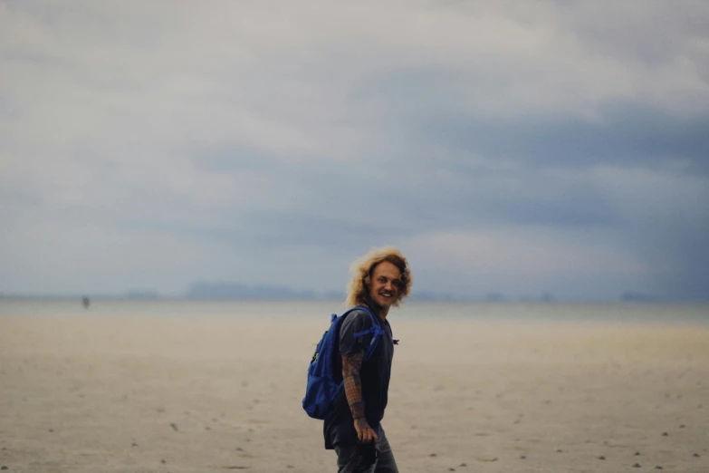 a man walking across the sand holding a surfboard