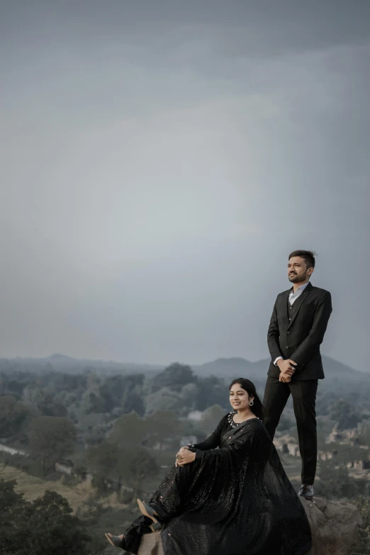 two people dressed formally and sitting on top of a hill