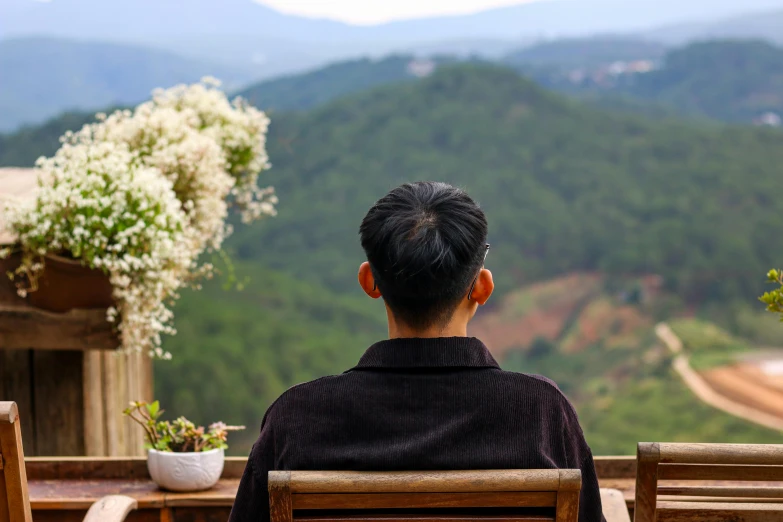 a person sitting down overlooking some flowers and mountains