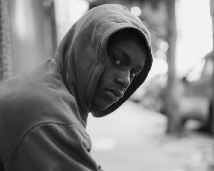 a hooded young black man is sitting on the curb