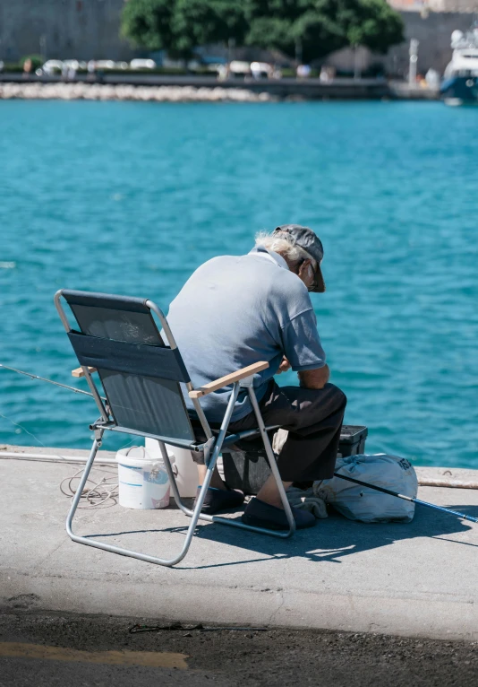 an old man is sitting on his chair at the edge of the water