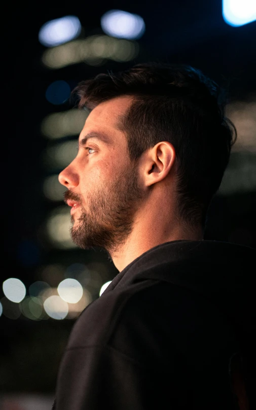 the profile of a man at night in front of a cityscape