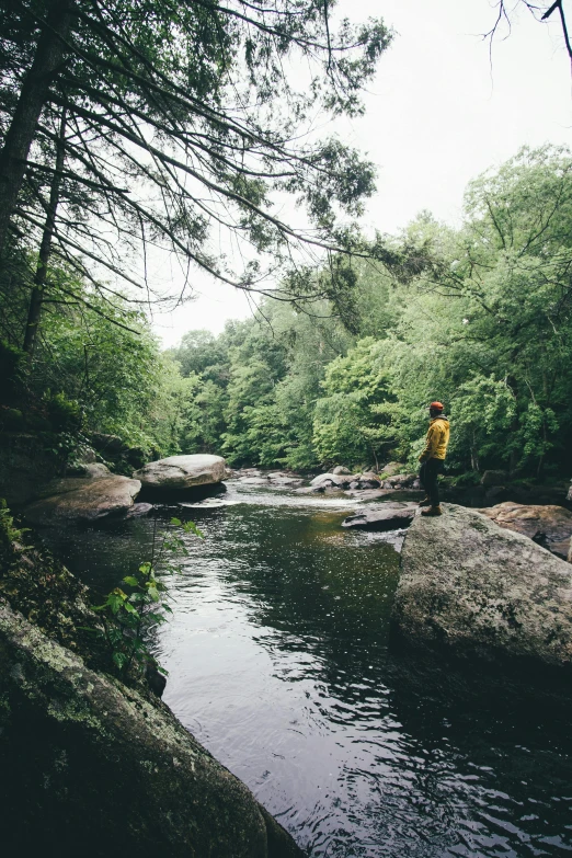 a person in yellow standing on rocks by a river