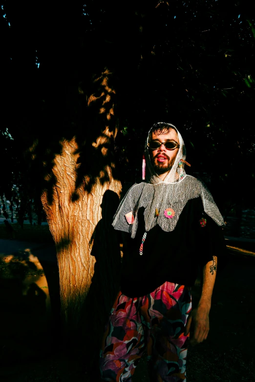 man wearing sunglasses and a scarf holding onto a tree