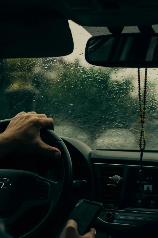 the hands are on the steering wheel of a car while riding through the rain