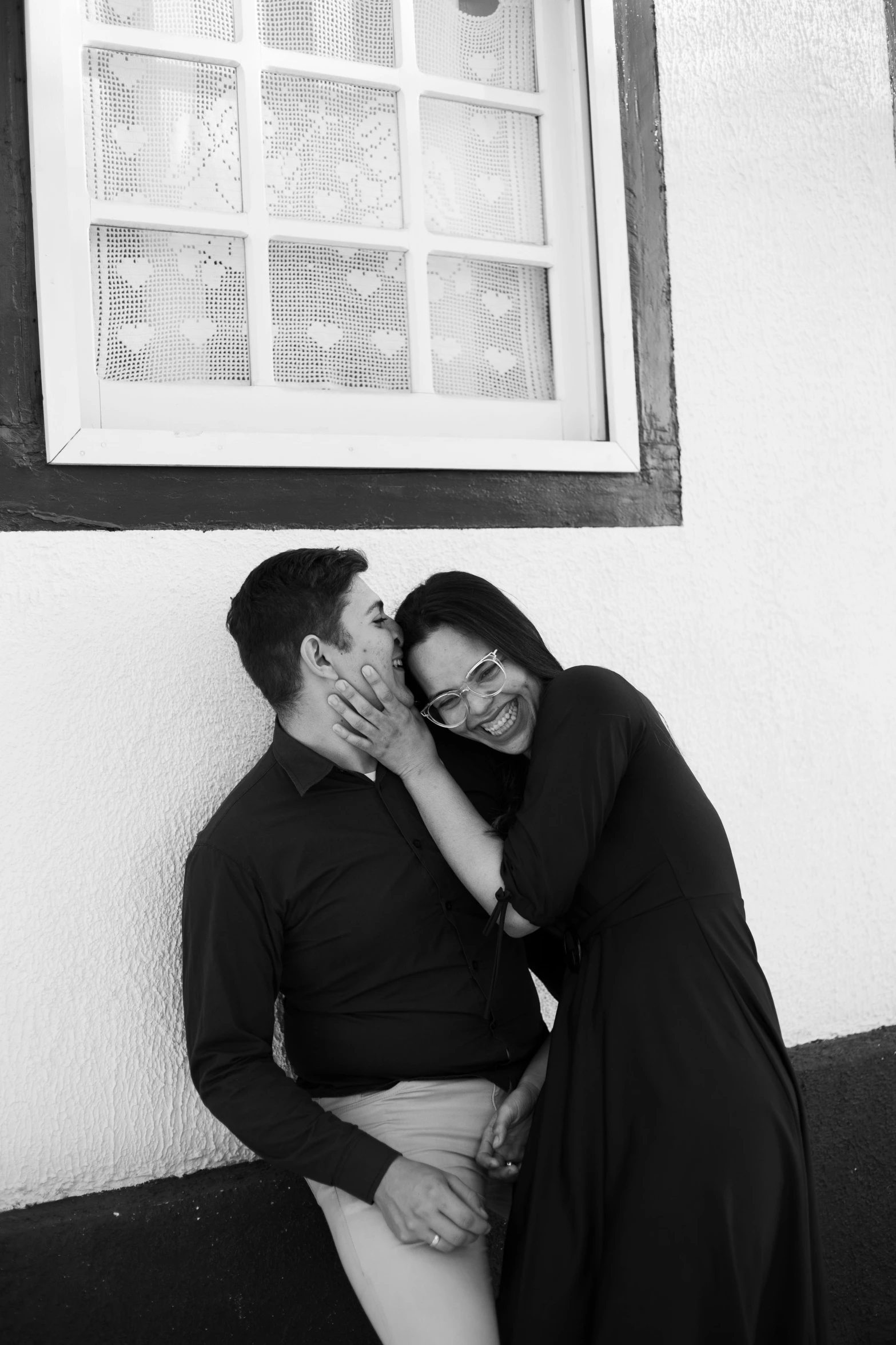 a man and woman leaning on a wall with their arms around each other