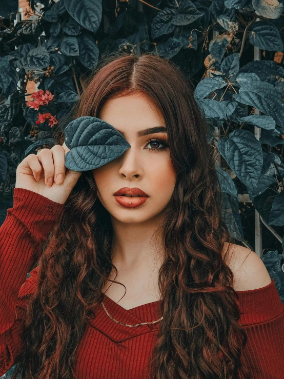 girl in a red off the shoulder top holds up a large leaf