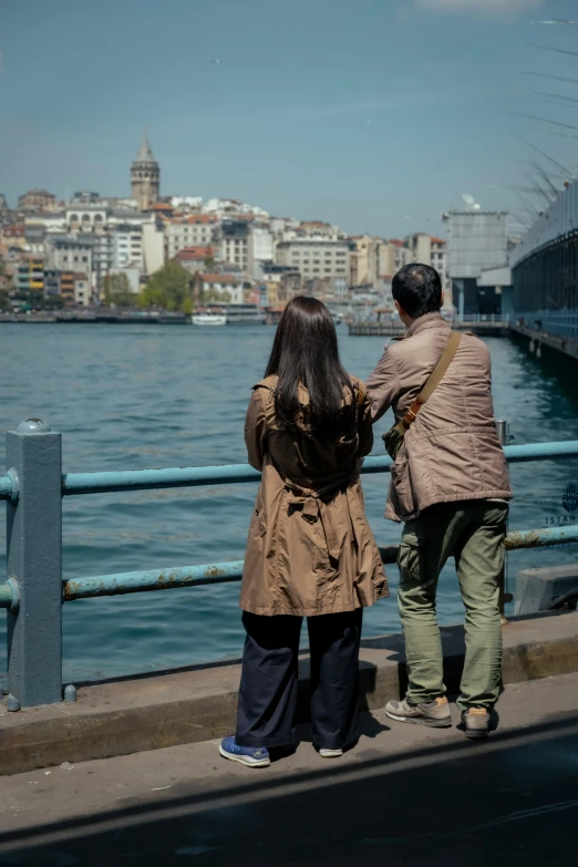 two people are walking near the water and some buildings