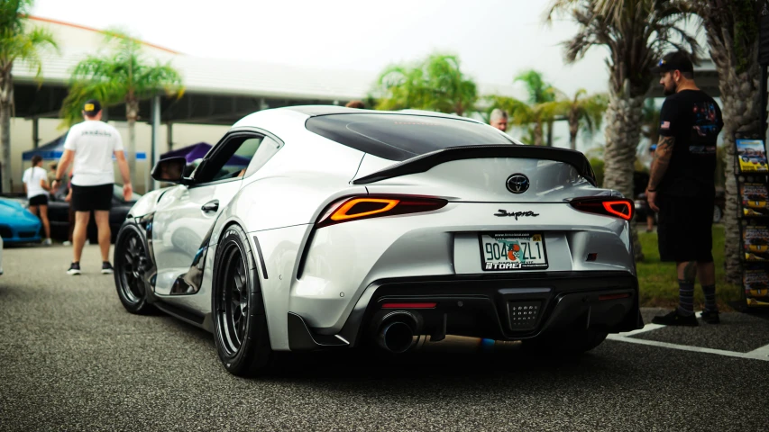 the rear end of a sports car with a lot of people around