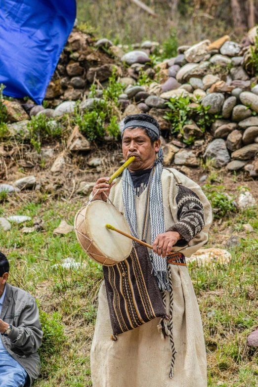 the man plays drums while another musician looks on