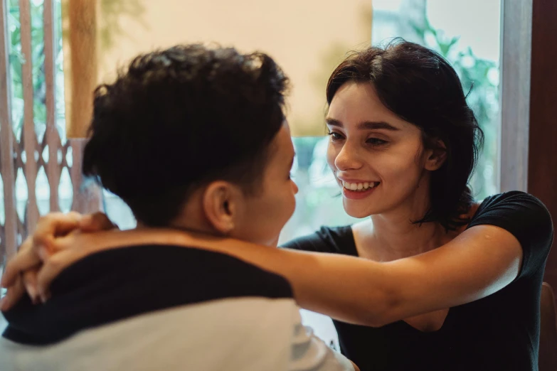 a woman smiles as another holds her hands around the shoulder