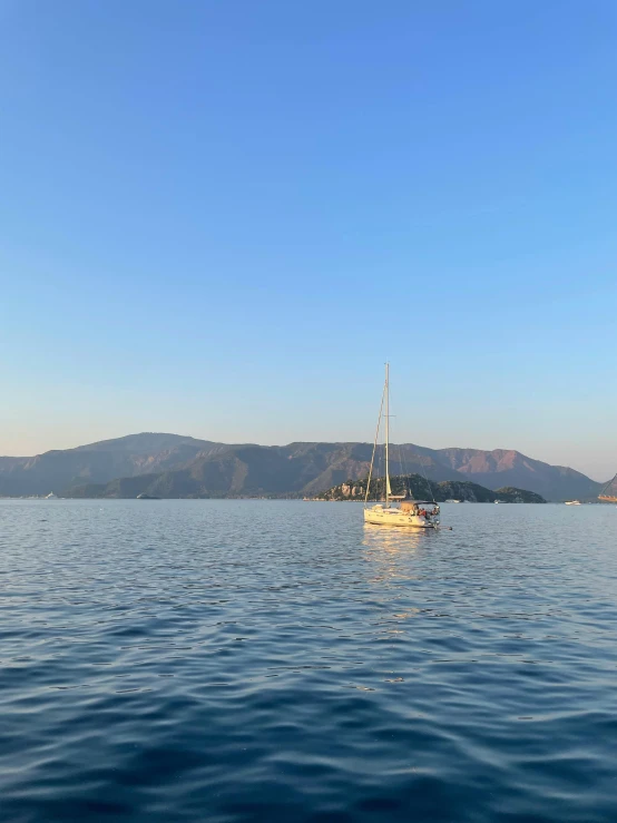 small sail boat out on the water with mountains in the distance