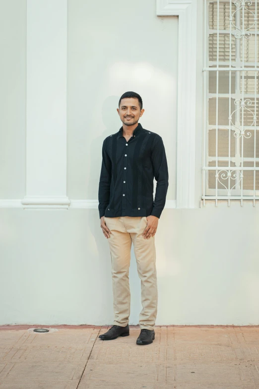 a man standing against a white wall in a black shirt