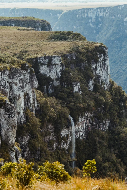 a mountain scene with tall cliffs, green fields and a waterfall