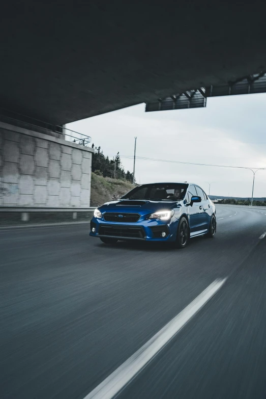 blue car driving down an empty highway underpass