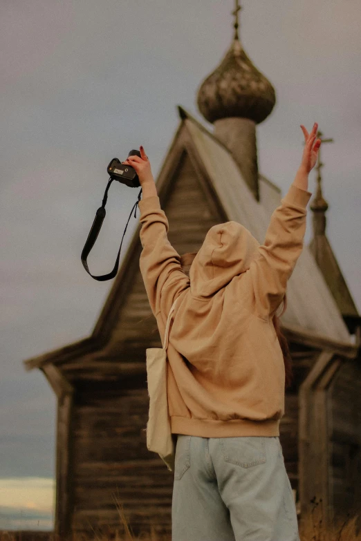 a man wearing a hoodie holding up his camera in front of an old church