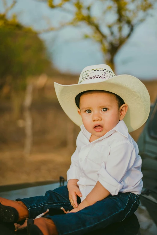 a toddler in white shirt and cowboy hat sits on top of pick up truck