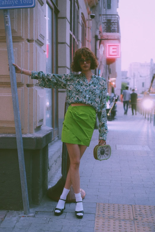 a woman in a green outfit leaning on a bus stop pole