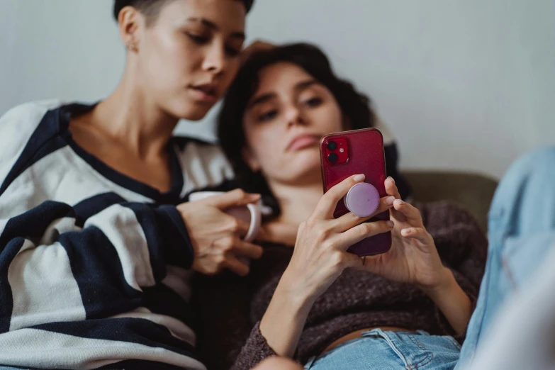 two women with their cellphones are on the couch