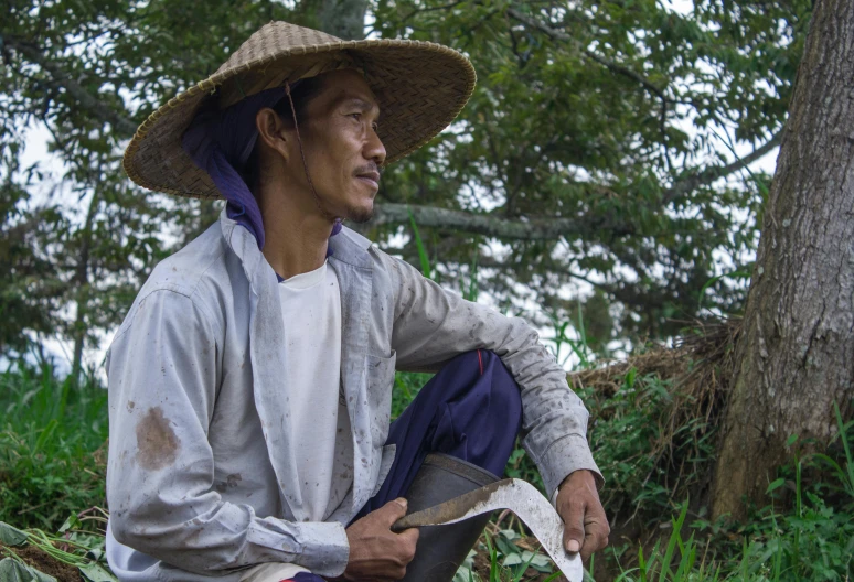 a man in white shirt and brown hat next to a tree