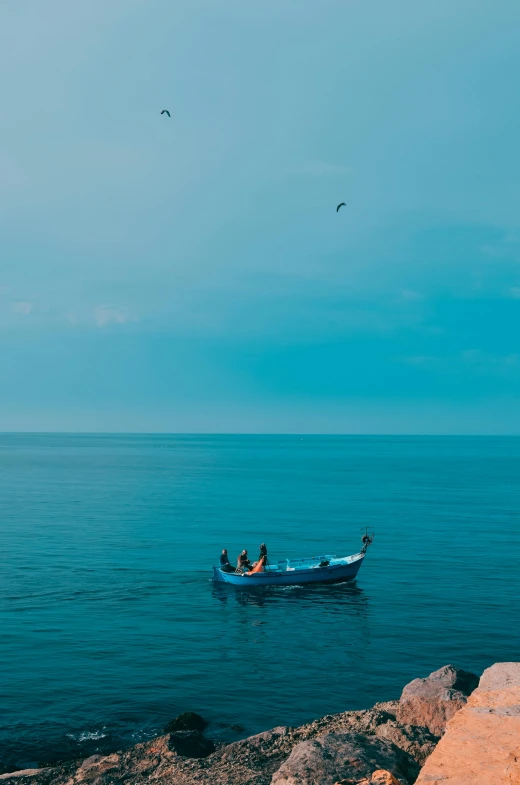 two boats on the ocean with rocks and seagulls flying in the sky