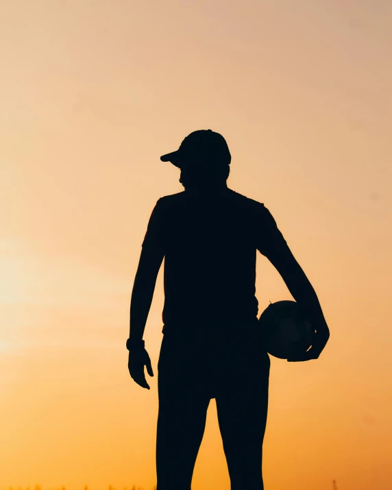 a person standing in front of a sunset holding a baseball