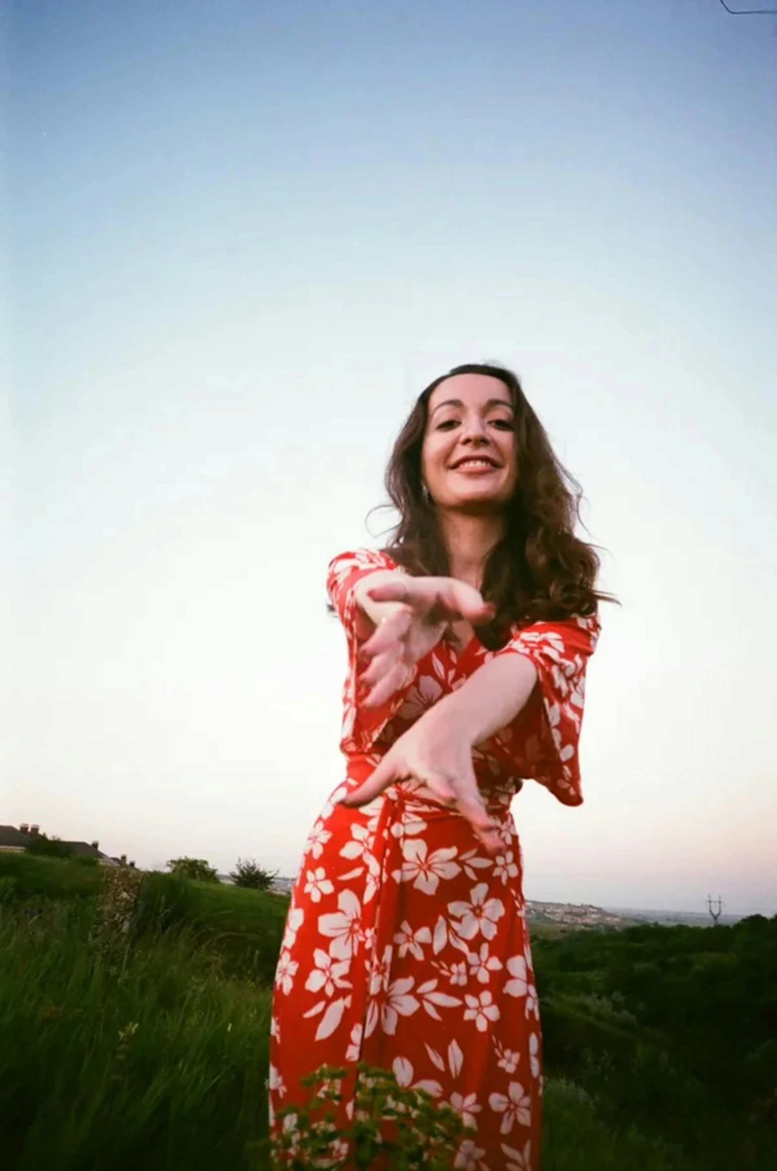 woman wearing red dress pointing at camera with sky in background