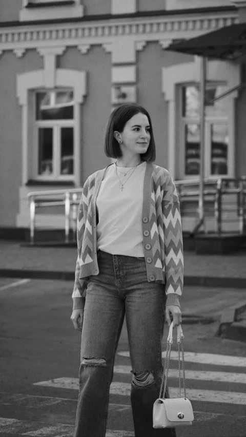 a woman in boyfriend jeans stands on the sidewalk with her handbag in front of an old brick building