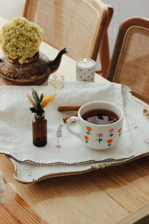 a teacup on a tray, with flowers and a tea can