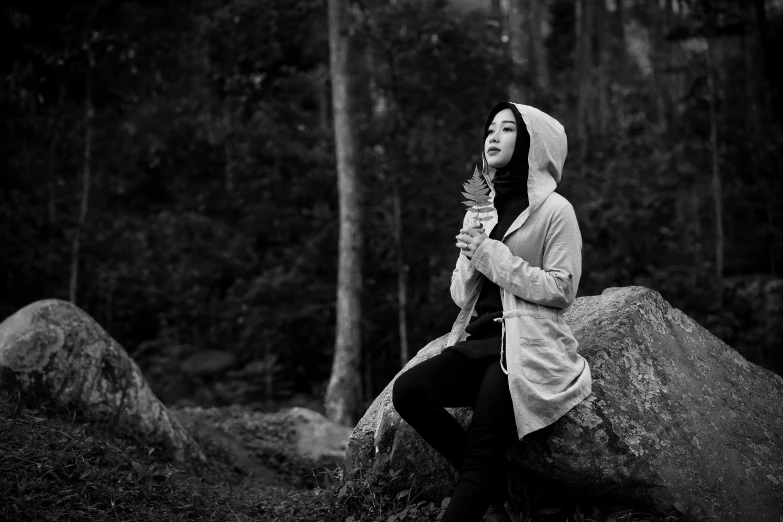 black and white image of a woman sitting on a large rock