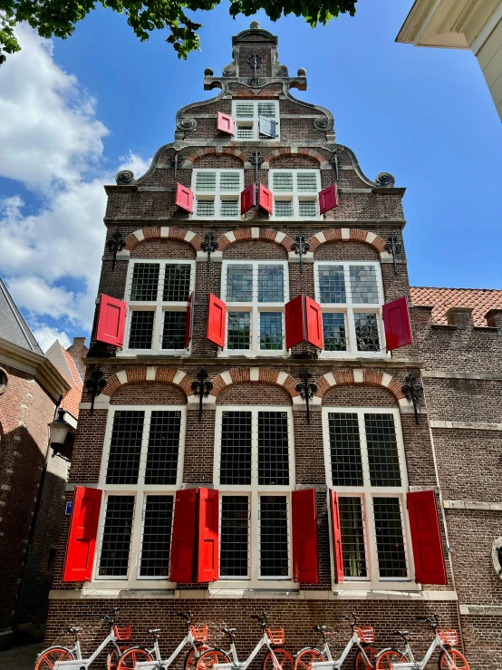 an old, red brick building has shutters open to let the sun see through