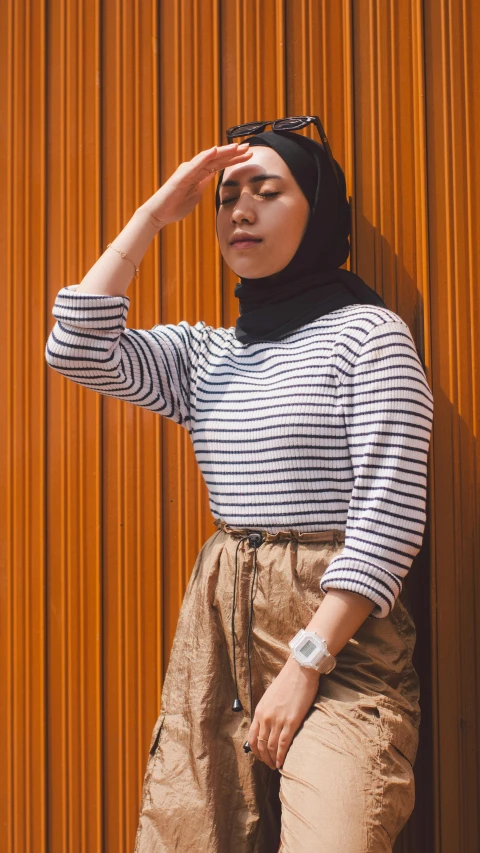 a woman standing against a brown wall with her hands on her head