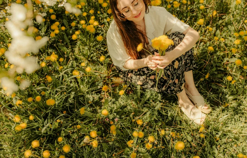 a girl sitting in the middle of a field holding flowers