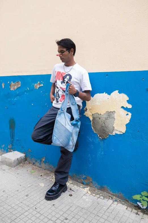 man standing against a blue wall with one hand on his bag