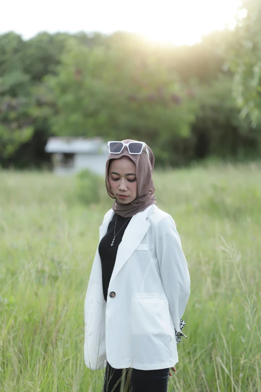 a woman standing in tall grass wearing a white jacket and a headscarf