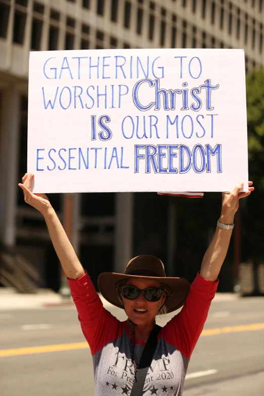 a woman holds a sign that says gathering to worship christ is our most essential freedom