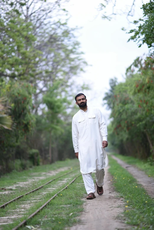 man in white dress walks down the tracks