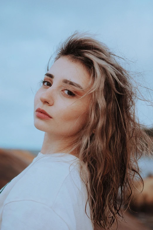 a young woman with frizz on her hair stands in front of the ocean