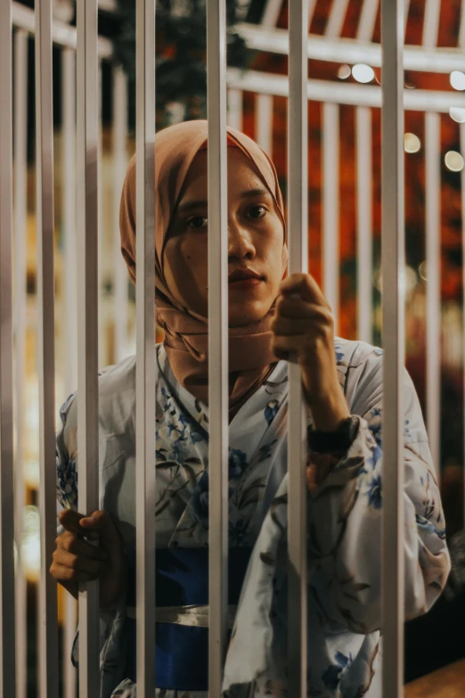 a woman in a hijab looks out from behind bars